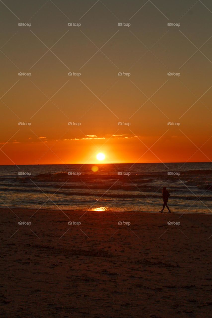 Lady walking along the beach at sunset.