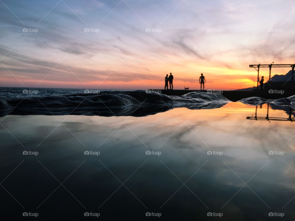 Three silhouettes standing above the sea on sunset. 