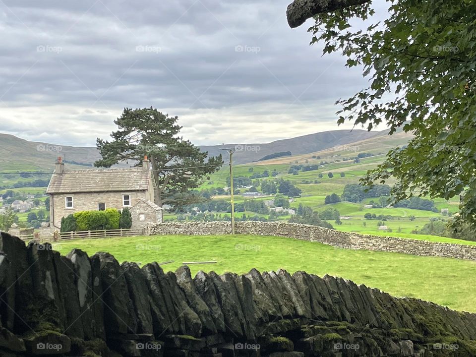 A charming country house nestled in the rolling hills of Yorkshire, England, with stone walls blending seamlessly into the landscape. Lush green grass stretches out, bordered by clusters of trees. Rolling hills create a peaceful, secluded backdrop.