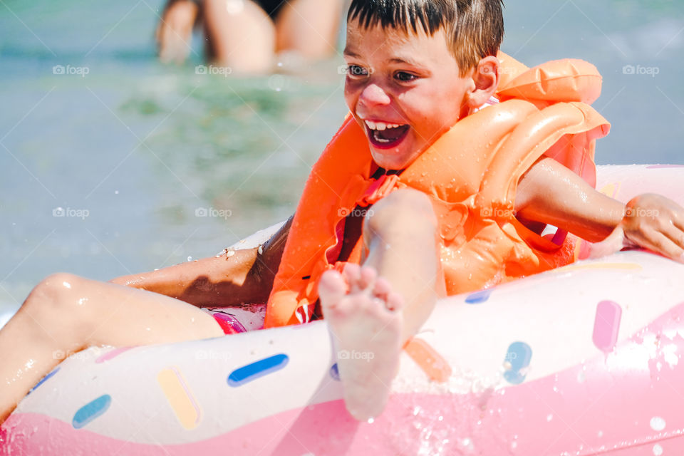Smiling happy boy in orange inflatable vest in the sea