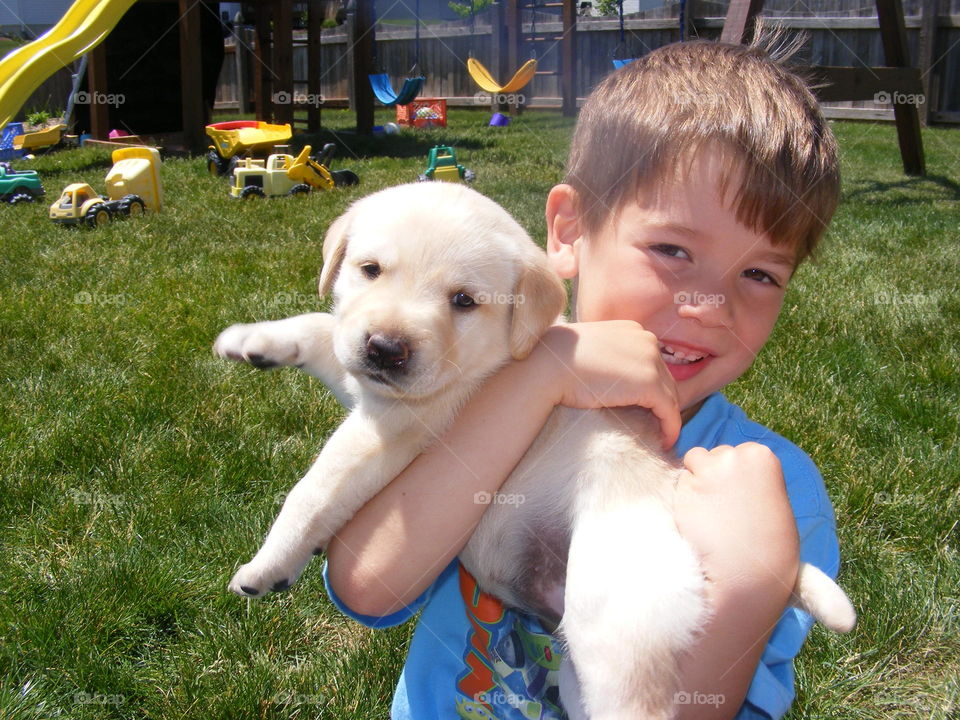 Young boy holding adorable yellow lab puppy while standing in the backyard