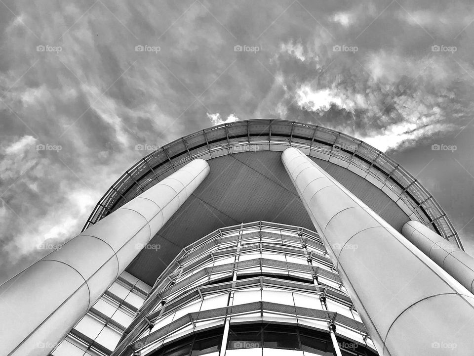 A building and sky captured in black and white from down to upside and there is a long poles towards the sky.