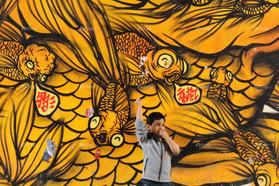 Kid standing by city wall mural in yellow color depicting dragon in Atlanta  
