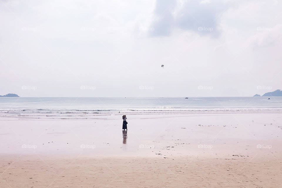 Young woman taking a photo of parasailing above the sea