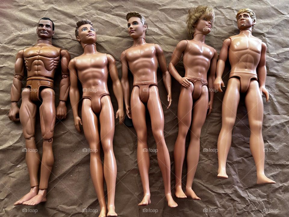 Various Ken dolls and other male dolls sans clothes on brown wrapping paper 