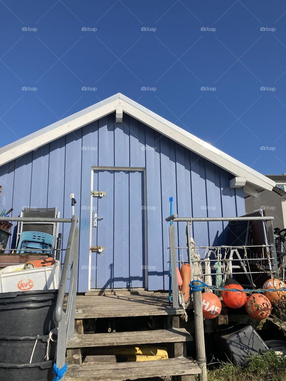 Blaues Holzhaus mit roten Boien davor. Blauer Himmel