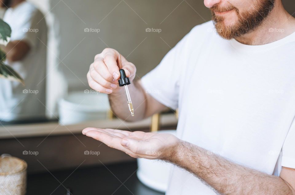 Adult handsome man with pipette with beard oil in bathroom at home