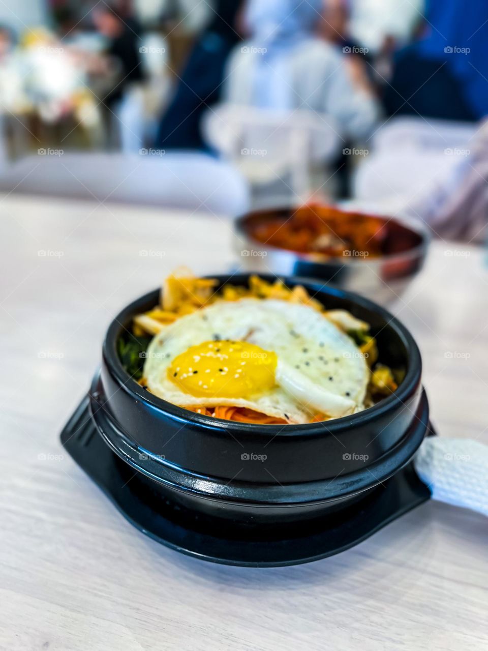 Korean food in a black bowl called bibimbap, egg and some beef and a lot of veggies 