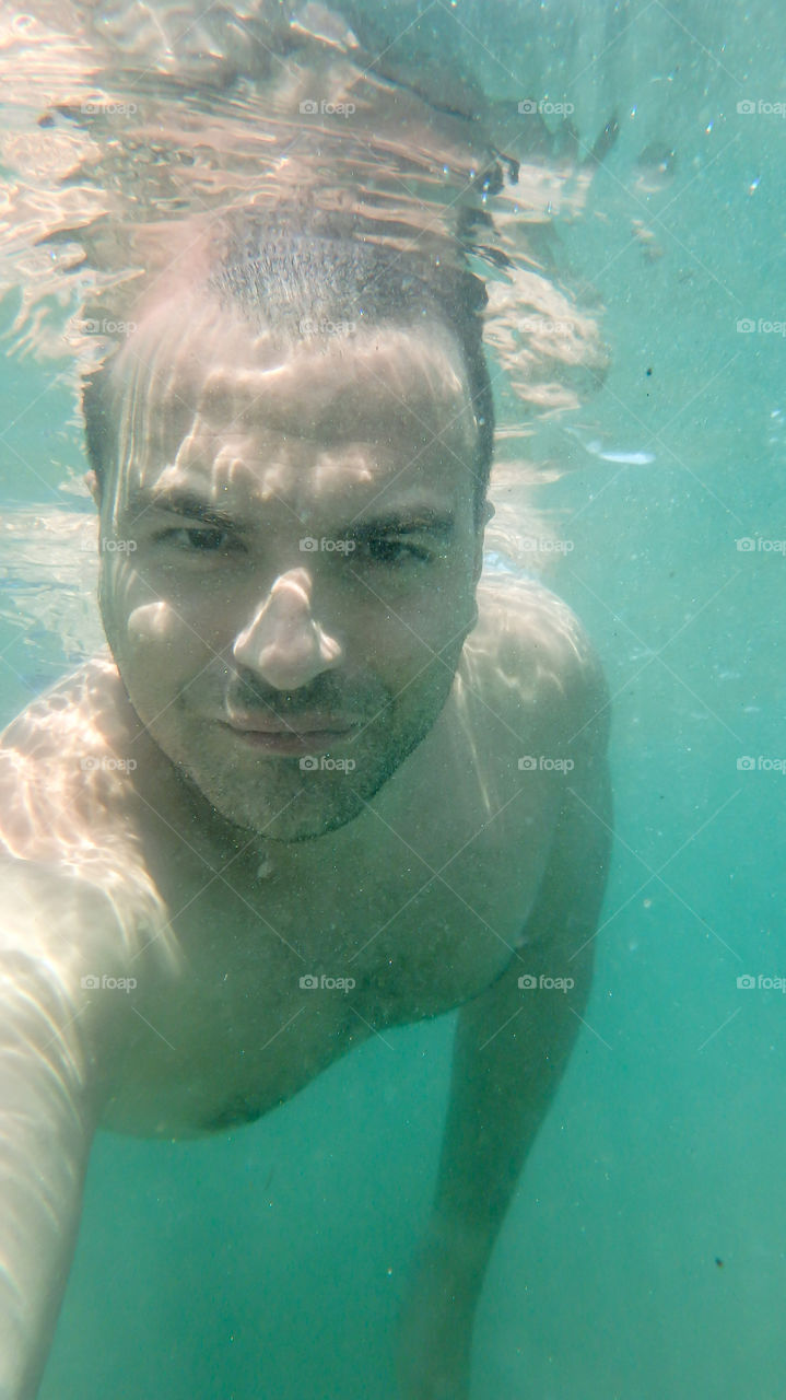 Man diving, man underwater smiling and relaxing in big blue sea