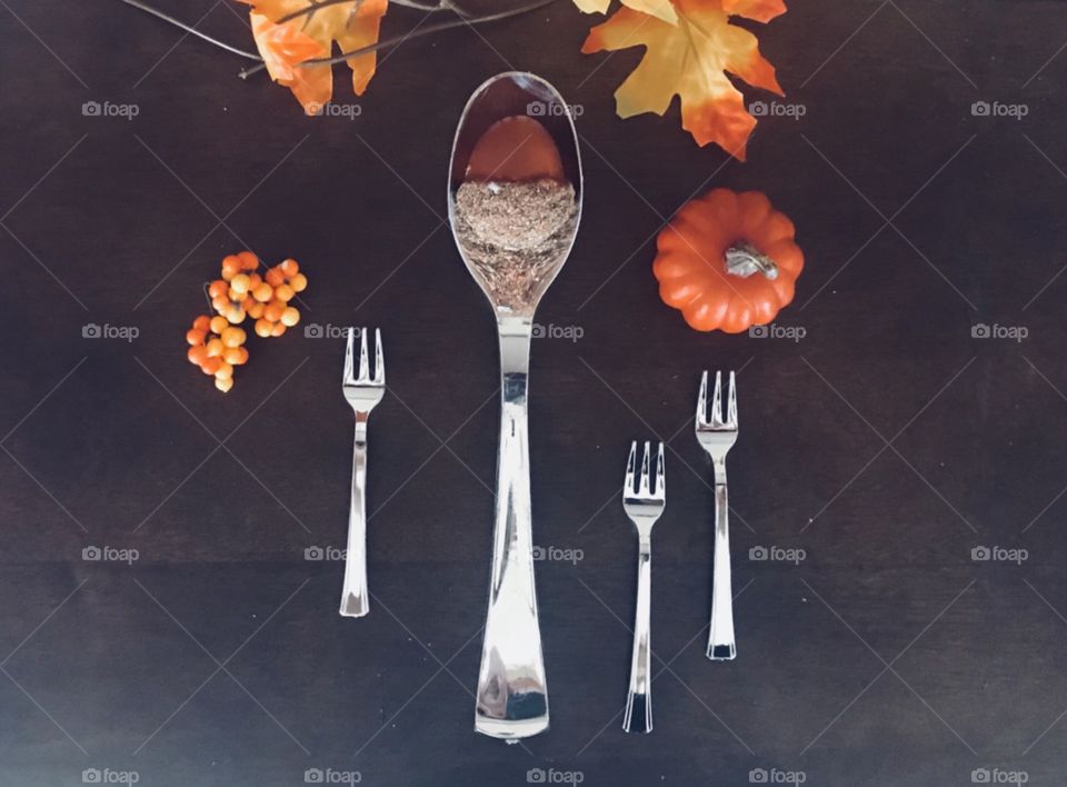 Beautiful table top display for the fall season large silver spoon with an acorn inside , surrounded by mini silver forks and holiday berries, mini orange pumpkin and autumn leaves- orange, red, brown, green and yellow, and gold