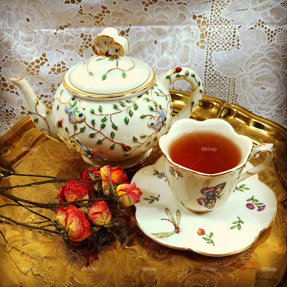 Fancy tea cup and teapot with dry roses and gold tray, lace backgeound