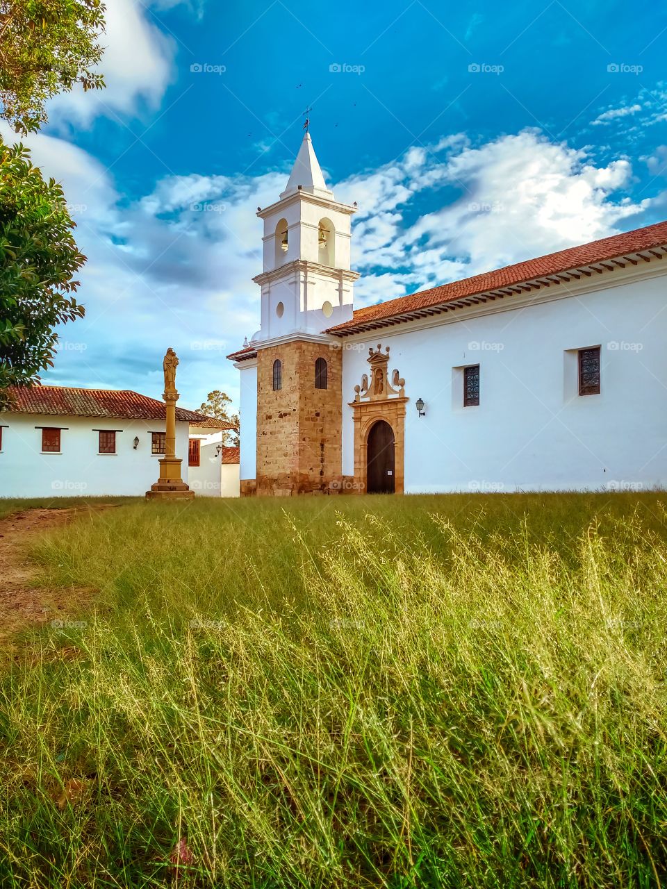 Villa de Leyva - Iglesia católica Nuestra señora del Carmen en Boyacá, Colombia. Catholic Church of Our Lady of Carmen. Sky blue, green forest. Vertical