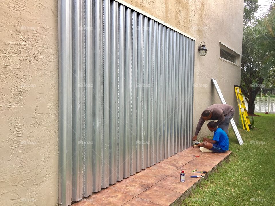 Father and son installing hurricane metal shutters on house, preparing for hurricane Matthew, Miramar, Florida