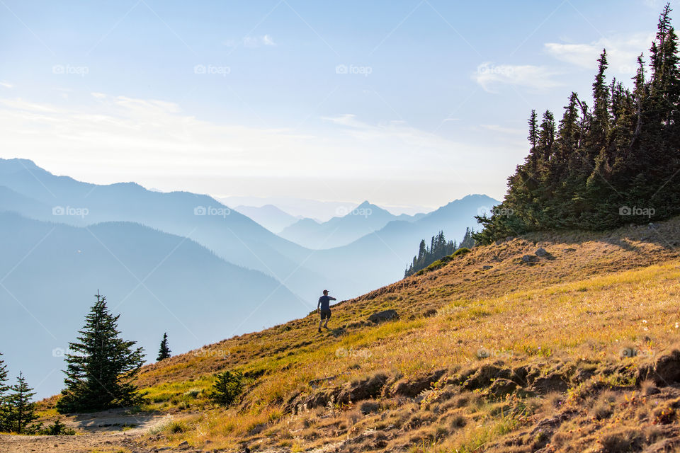 A hiker trekking up a steep mountain ridge with endless layers of beautiful hazy mountain peaks in the distance. 