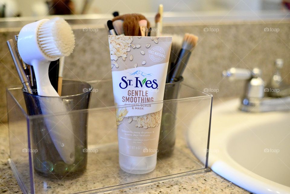 St Ives cleanser in a container on a bathroom counter next to a sink, with brushes in the background 