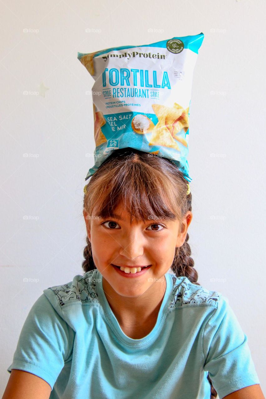 Cute happy girl balancing bag of chips on her head