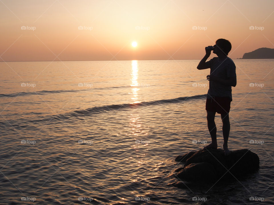 Silhouette of man drinking can at sunset