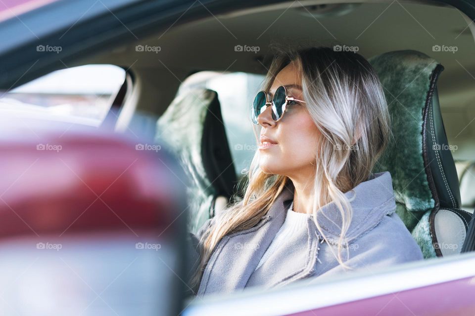 Young stylish woman with long blonde hair and sunglasses driving car