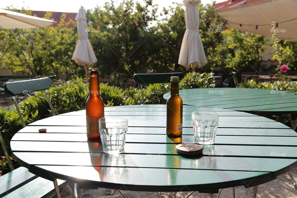 Glass bottles and drinking glasses on a wooden table outdoors at s garden cafe 