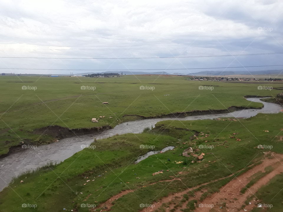 A flooded stream flows through the grassland with cloudy and cloudy skies over the riverside.