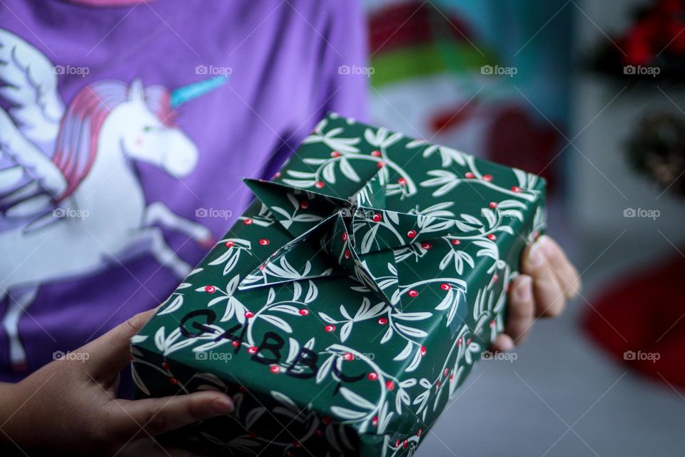 Child in a pajamas with unicorn is holding her Christmas present