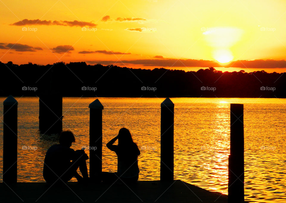Silhouette of couple sitting on pier at sunset