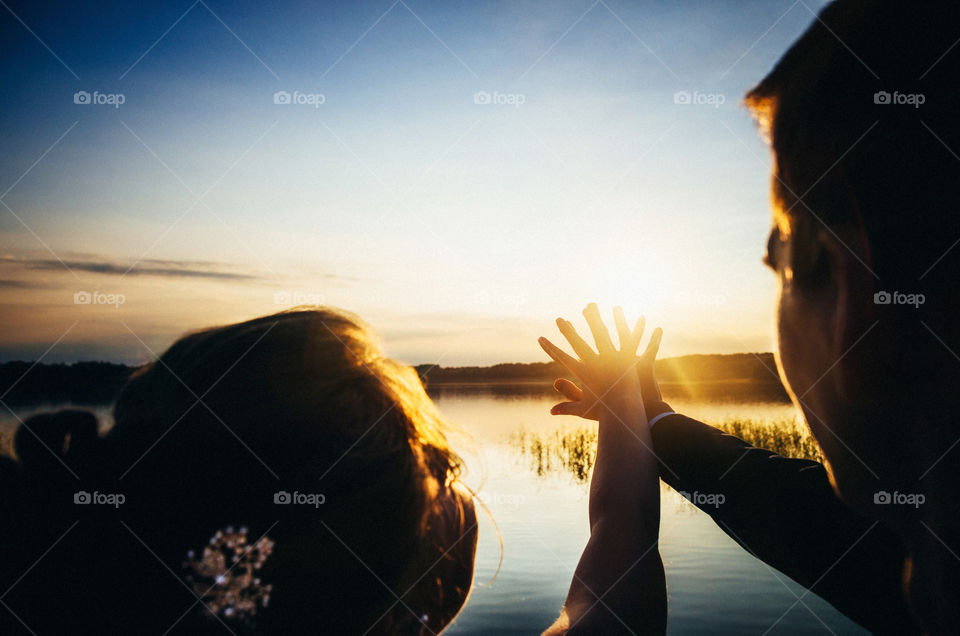The bride and groom crossed hands against the sun. Wedding concept at sunset