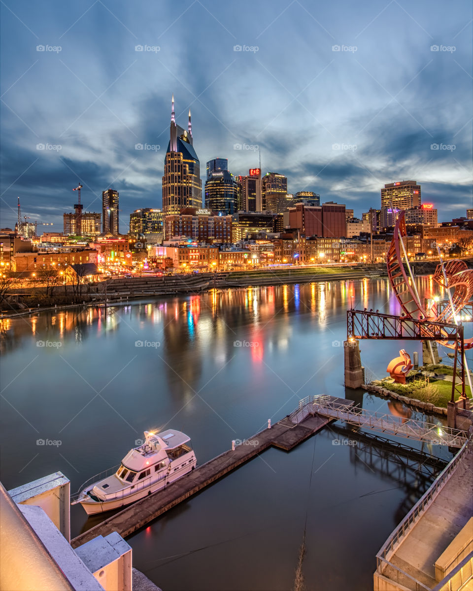 Cityscape of downtown Nashville Tennessee as seen from across the Cumberland River. Skyline reflections in the river as clouds streak across the sky. 