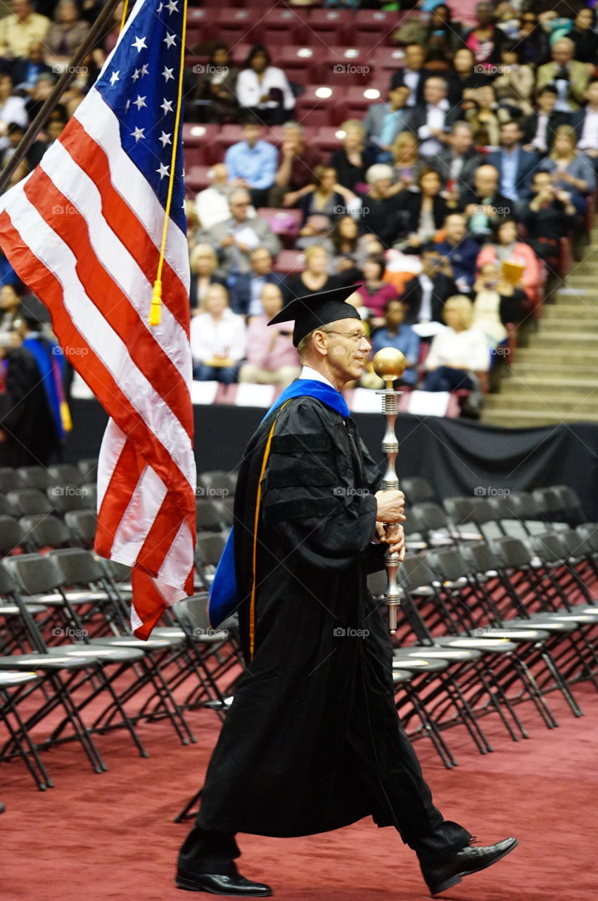 Man walking in graduation gown near flag