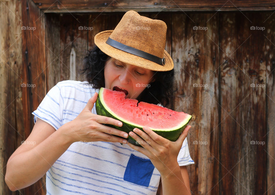 A woman with summer hat eating a watermelon slice outdoor