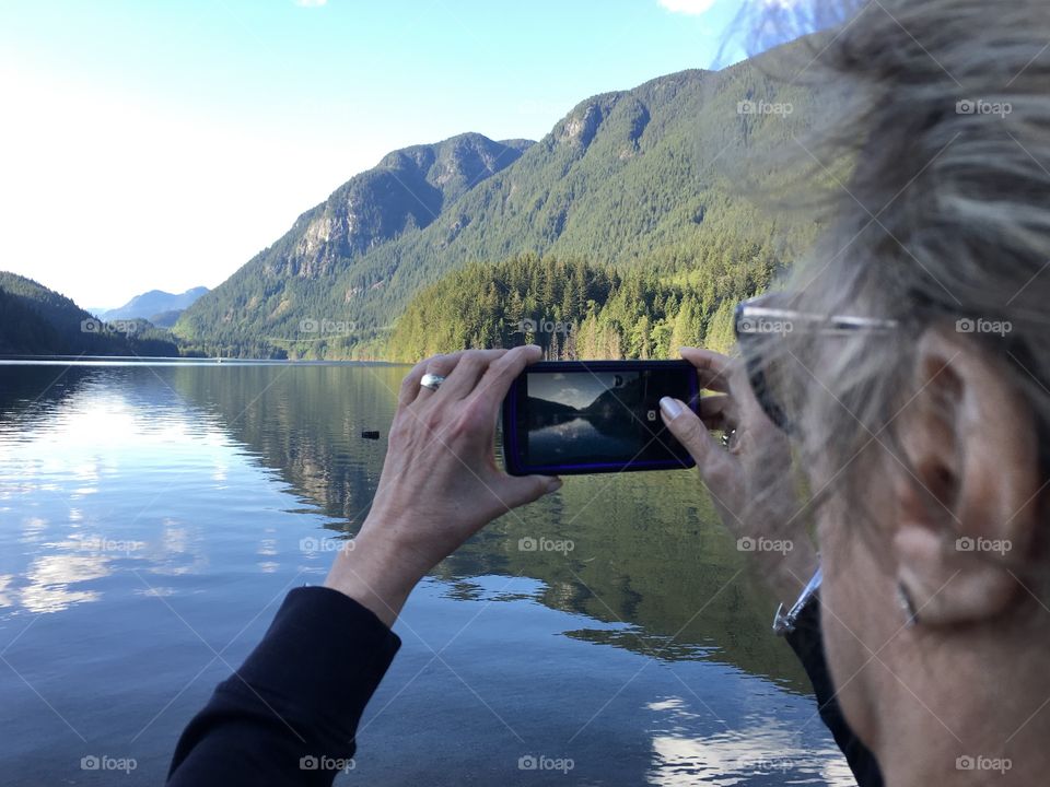 Woman with smartphone photographing scenic lake and reflections head profile