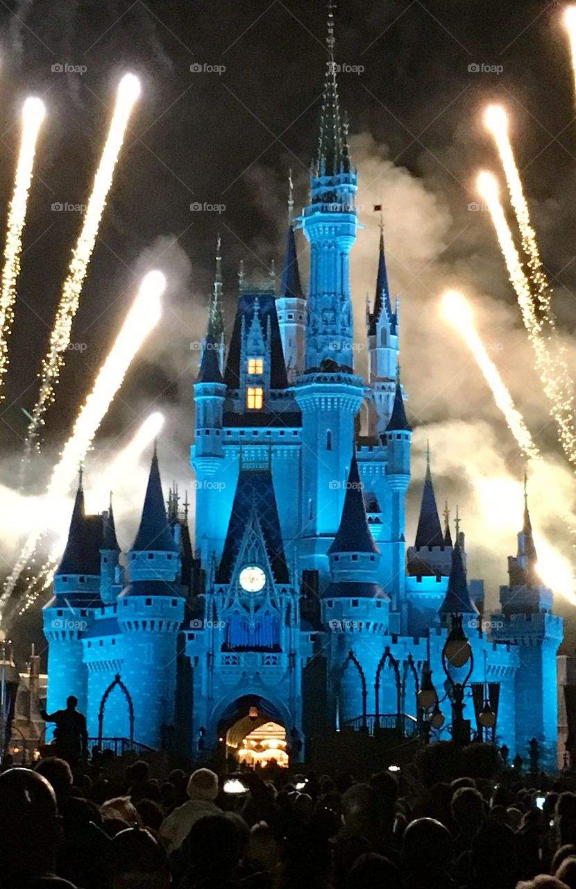 Cinderella’s Castle in Disney World lit up blue with fireworks behind it 