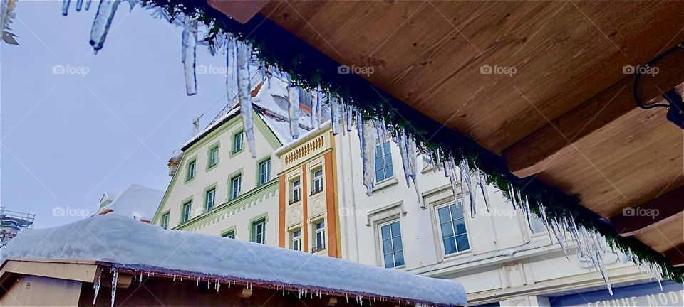 The buildings peaking out from under the roof of one of the sheds of the “Christkindlmarkt”, a Christmas fair in “Straubing”, “Bavaria”, Germany are lining the “Theresienplatz”, a main square named after a Bavarian queen. 2023. Hypnotic Productions