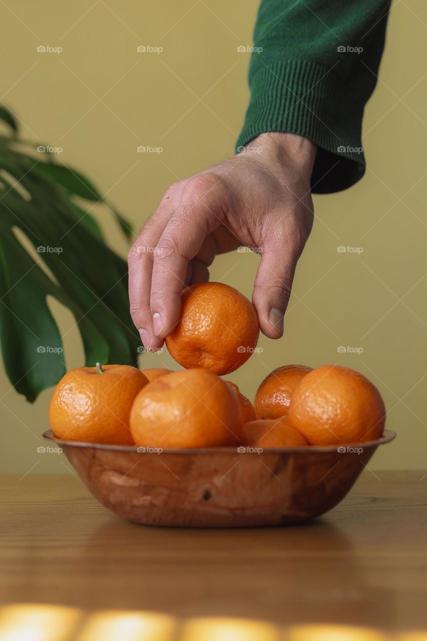 Cropped hand of man holding orange fruit on table .