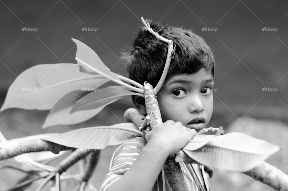 Black and white image of village kid carrying tree branch.