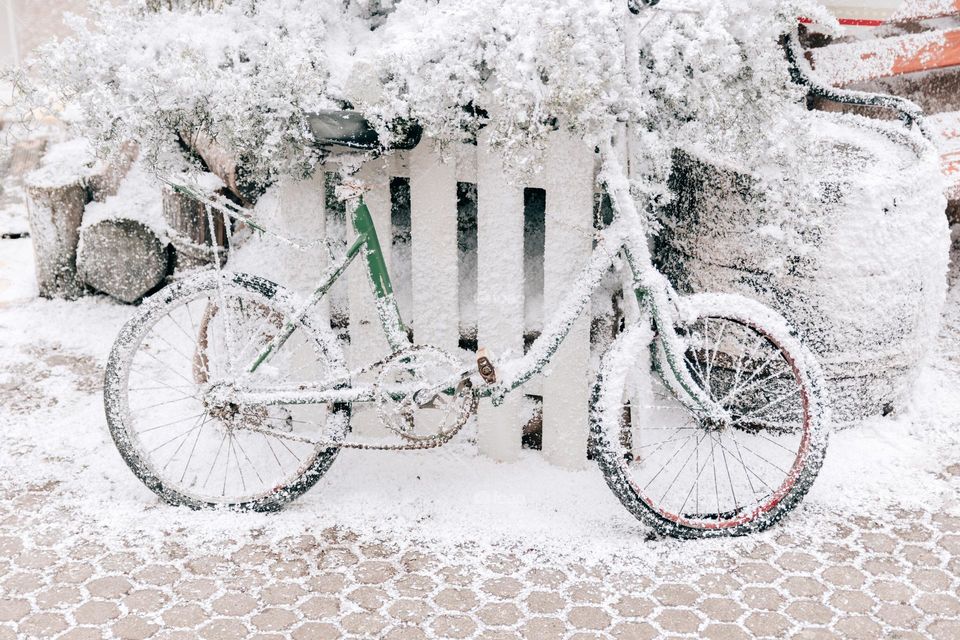 Vintage bicycle covered with snow leaning on white fence