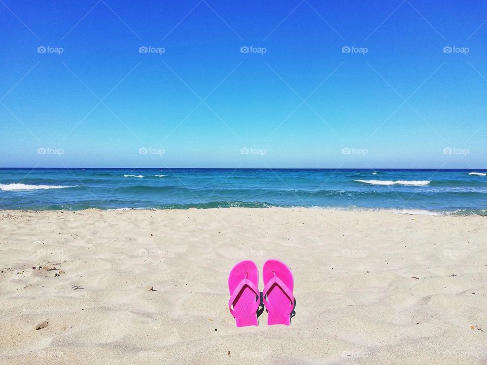 pink flip flops dipped in the sand on the deserted beach