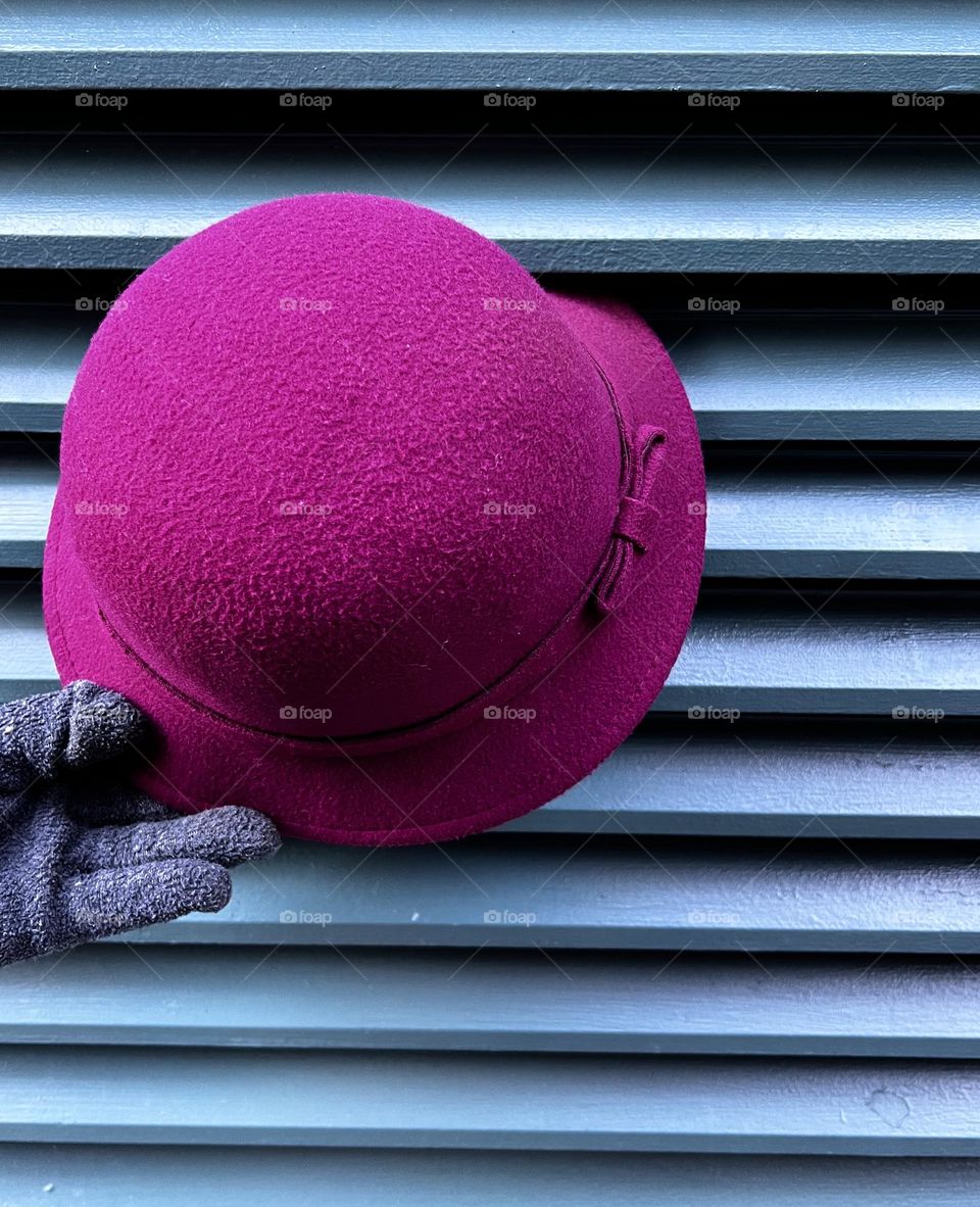 A person holding a magenta hat with dark green background.