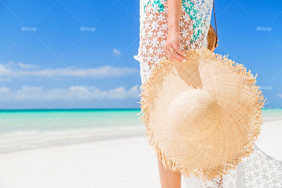 Stylish fashionable woman wearing tunica and holding straw hat on the beach 