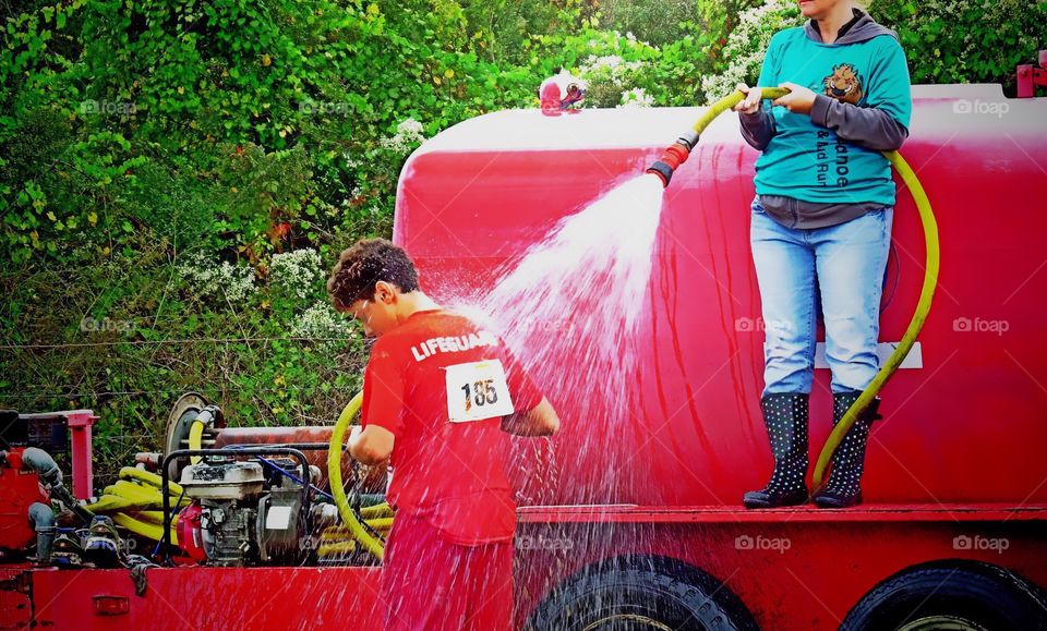 A young boy cools off under a fire truck hose after a foot race.