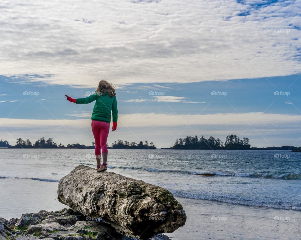 Girl walks and balances on huge piece of driftwood at scenic coastline of Vancouver Island 