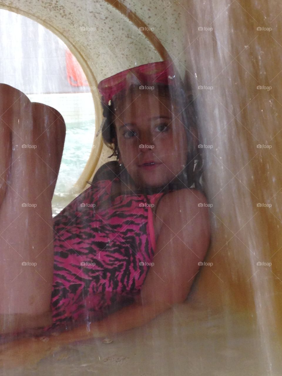 Through the waterfall. View of a girl sitting in a tunnel behind a waterfall at an indoor water park