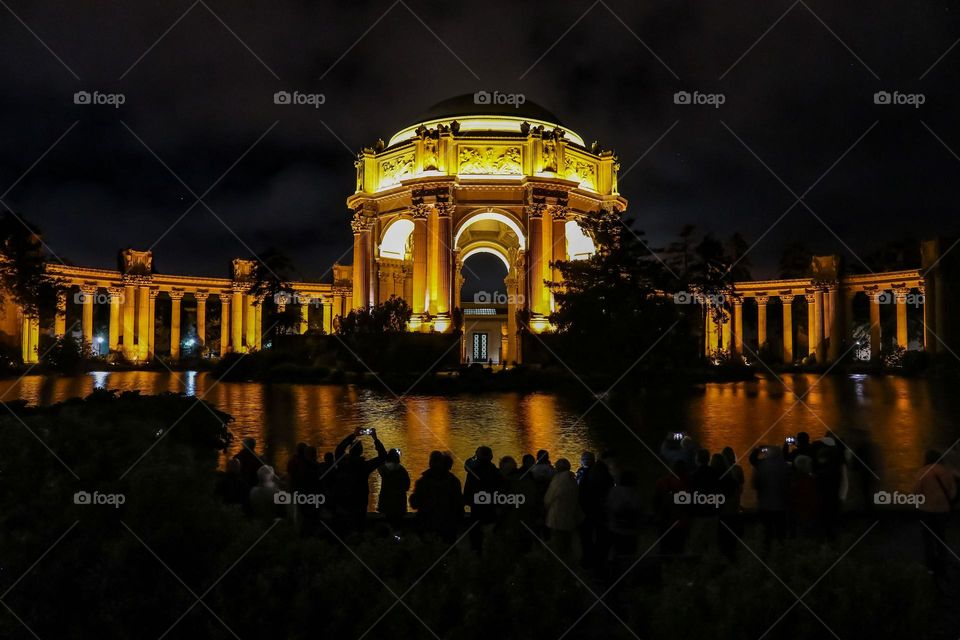 Crowd of people gathering in front of the Palace of Fine Arts in San Francisco California at night to watch the illumination of the lights on the buildings reflecting and shimmering in the water of the lagoon on a beautiful night.