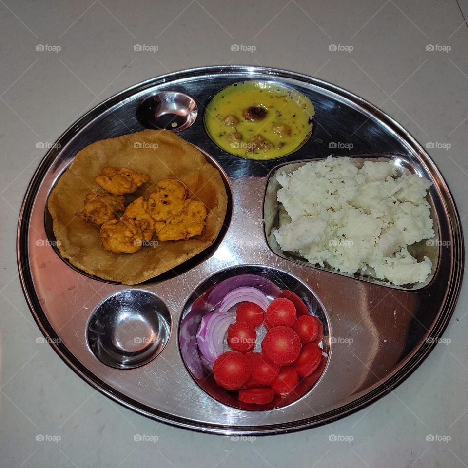 India food: curry pakoda, fritters, rice, puri, and a healthy corner of salad with carrot and onion.