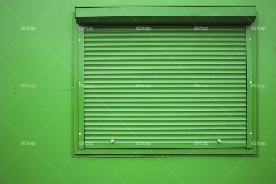 Green window shutter on green wall
