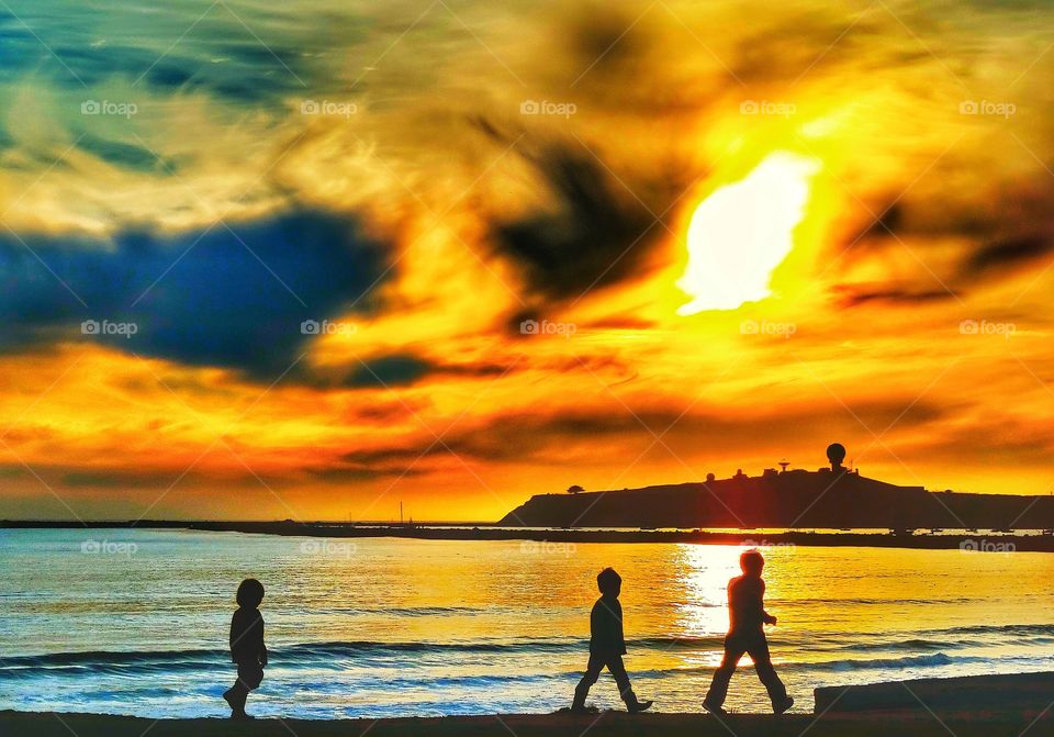 Children Walking Along A Beach At Sunset