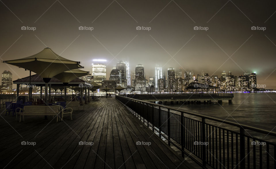 Skyline of New York City from a wooden walkway by the Hudson river in New Jersey on a foggy night