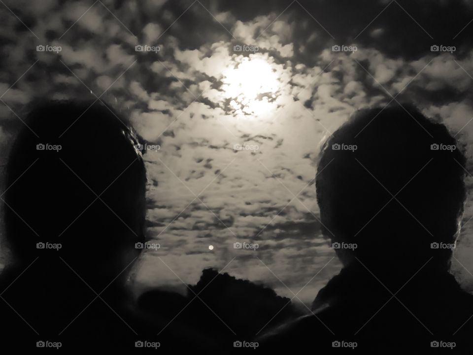 Two men gazing at the bright full moon. The moon  behind clouds