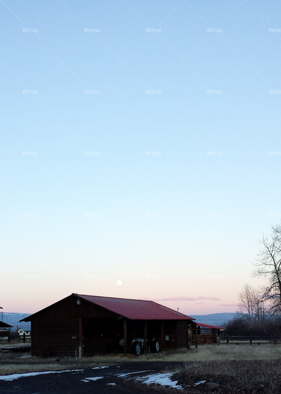 Moon over barn during sunset