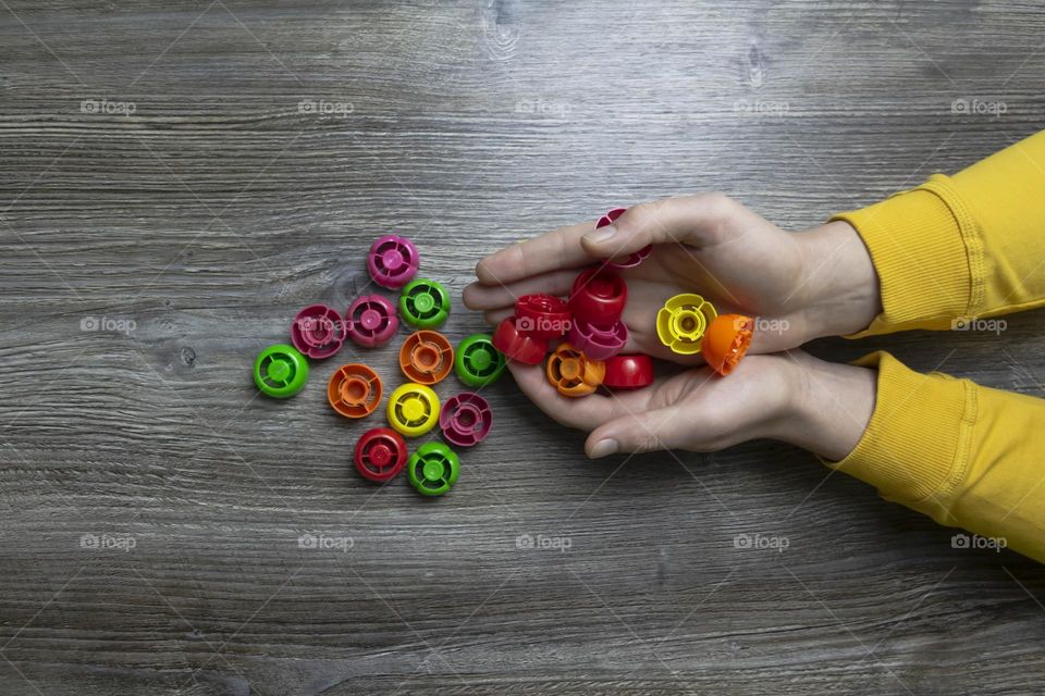 We collect garbage, plastic plugs and plastic to save our planet, nature and the environment. Men's hands lie on a gray wooden surface, which is used as a background or a surface with incident light.